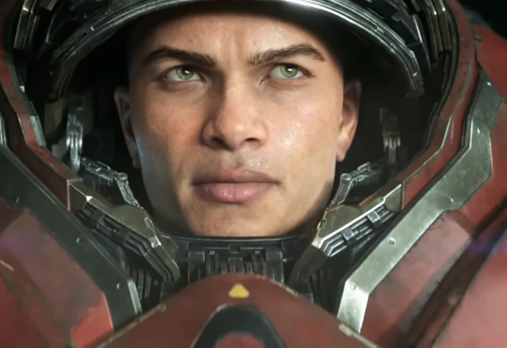 Primer plano de un hombre con ojos verdes y piel morena clara, ataviado con un traje de armadura futurista rojo y gris, reminiscente de un marine Terran de Starcraft. Su mirada seria y decidida ilustra la intensidad del próximo título de la saga.