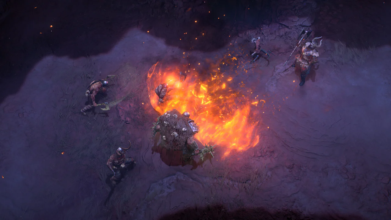Vista cenital de tres guerreros con armadura combatiendo contra un gigantesco monstruo de fuego y roca en un entorno oscuro y desolado, con chispas incandescentes volando por el aire, ilustrando la intensa acción de Diablo V.
