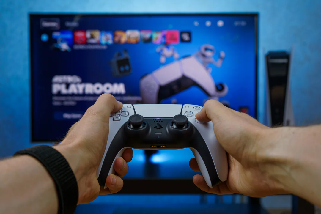 Manos sosteniendo un mando DualSense frente a un televisor que muestra la interfaz de PlayStation 5, ilustrando la experiencia de usuario en la era del ecosistema digital.
