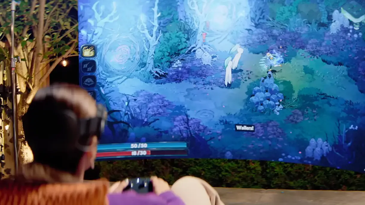 Una persona con un casco de realidad virtual, que representa el Steam Frame, juega a un RPG de fantasía isométrico en una gran pantalla curva exterior, mostrando un entorno boscoso azulado y elementos de HUD como barras de estado y habilidades.