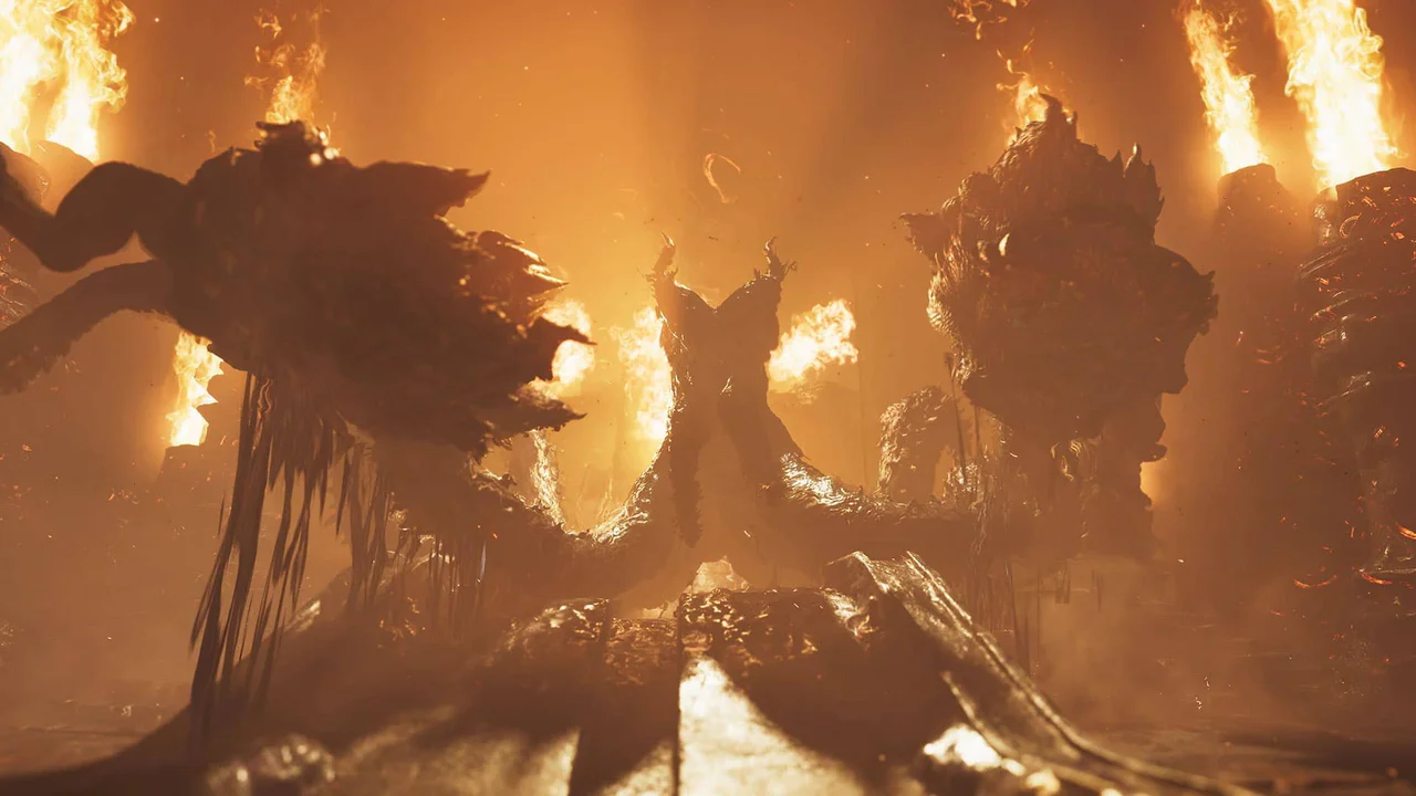 Un colosal monstruo, posiblemente un dragón ancestral o una bestia épica, emerge imponente en un paisaje infernal bañado por intensas llamas y humo naranja. La criatura de silueta oscura y múltiples apéndices domina el centro, reflejando la escala épica y los desafíos del mundo de Monster Hunter Wilds.