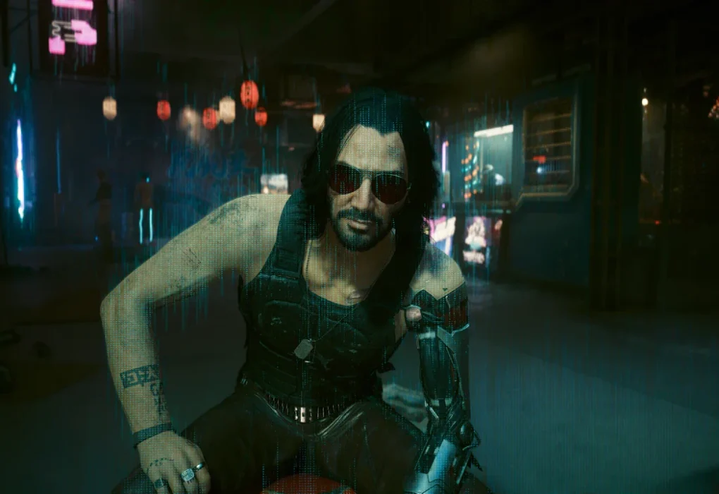 Johnny Silverhand, personaje icónico de Cyberpunk 2077, sentado bajo la lluvia en un callejón futurista de Night City, con gafas de sol y su brazo cibernético. La escena evoca la atmósfera del juego que ahora tendrá un mod multijugador.