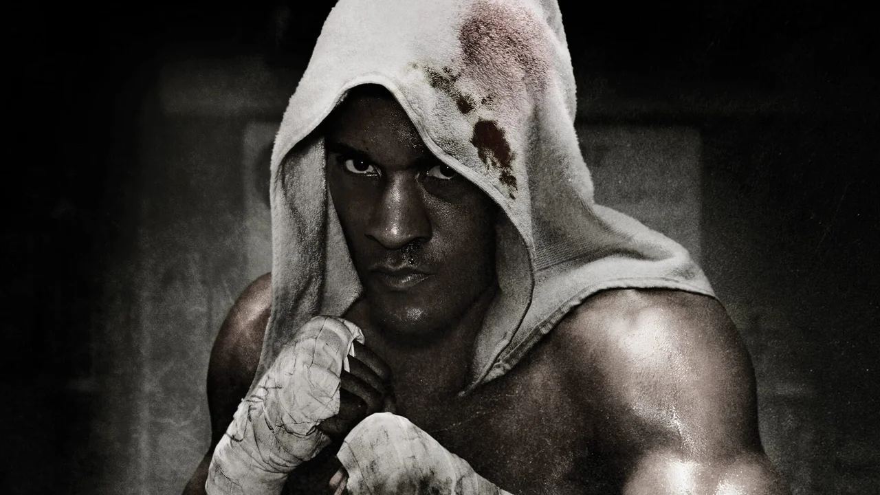 Retrato en blanco y negro de un boxeador con vendas en las manos y una sudadera con capucha salpicada de sangre, mirando directamente a cámara con una expresión determinada que captura la esencia cruda del boxeo y la serie Fight Night.