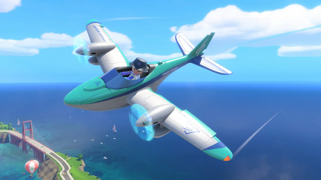 Un hidroavión blanco y azul turquesa vuela invertido sobre la Isla Wuhu, con su icónico puente colgante y globos aerostáticos a lo lejos, ilustrando la actividad aérea en el próximo Nintendo Switch Sports Resort.